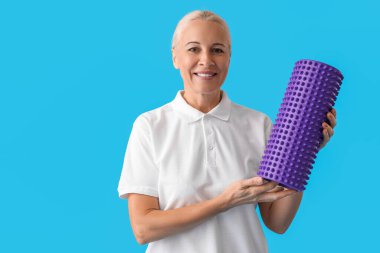 Mature physiotherapist with foam roller on blue background