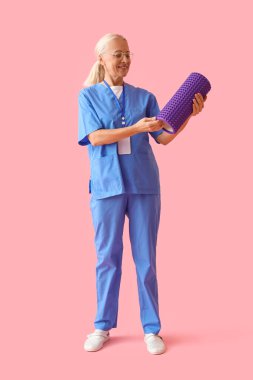 Mature physiotherapist with foam roller on pink background