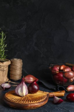 Wooden board with red onion on dark background