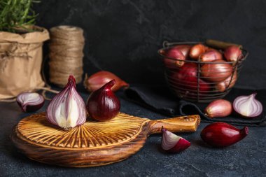 Wooden board with red onion on dark background