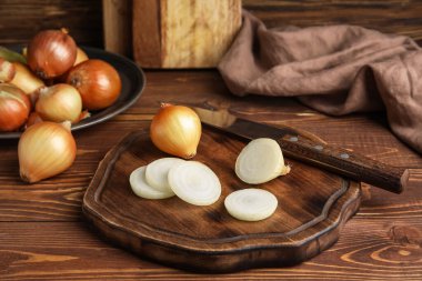 Board with fresh cut onion and knife on wooden background