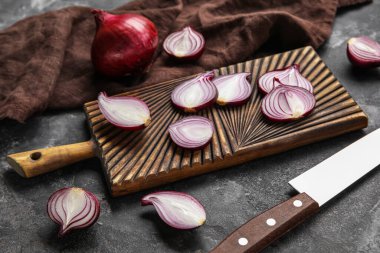 Wooden board with cut red onion on dark background