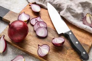 Wooden board with cut red onion and knife on table, closeup