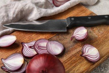 Wooden board with cut red onion and knife, closeup