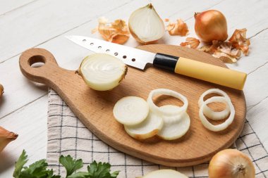 Board with cut onion and knife on light wooden background, closeup