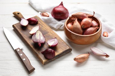 Wooden board and bowl with red onion on light wooden background
