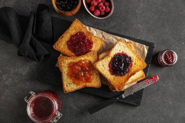 Composition with wooden board of tasty toasts and jam on dark background