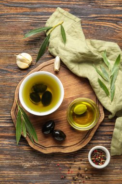 Composition with bowls of fresh oil, olives and spices on wooden background