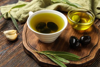 Board with bowls of oil and olives on wooden table, closeup