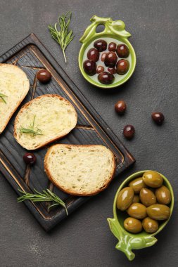Composition with bowls of olives and fresh bread on dark background