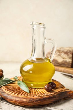 Wooden board with decanter of fresh olive oil on light background, closeup