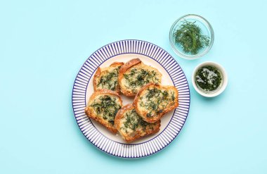 Plate with slices of toasted garlic bread, oil and dill on color background