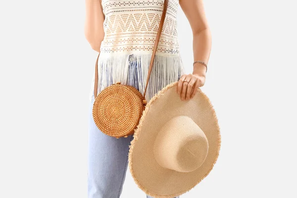 Woman holding stylish hat and rattan bag on light background