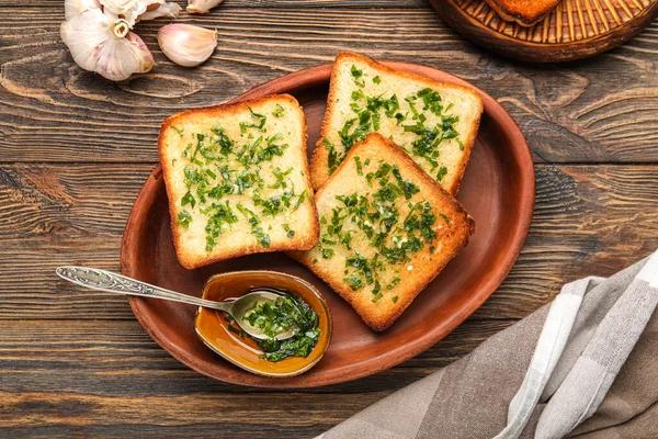 Plate with toasted garlic bread and oil on wooden background