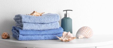 Stack of clean towels, sea shells and soap on table in bathroom