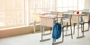 Interior of modern empty classroom with hanging backpack on desk