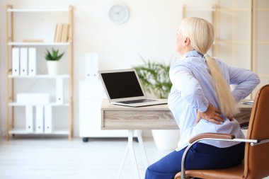 Mature businesswoman suffering from back pain in office