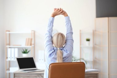 Mature businesswoman with back pain doing exercise in office
