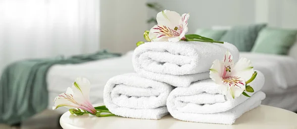 Clean soft towels with flowers on table in bedroom