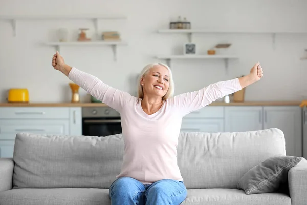 Mature woman with back pain doing exercise on sofa in kitchen