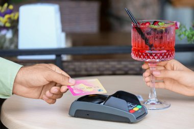 Man paying with credit card via payment terminal at table in cafe, closeup