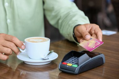 Man paying for coffee with credit card via payment terminal at table in outdoor cafe, closeup