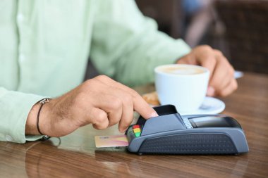 Man paying for coffee with credit card via payment terminal at table in outdoor cafe, closeup