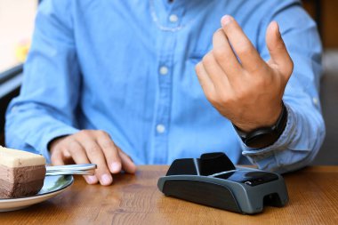 Man paying for cake with smartwatch via payment terminal at table in cafe, closeup
