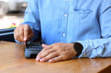 Man paying with credit card via payment terminal at table in cafe, closeup