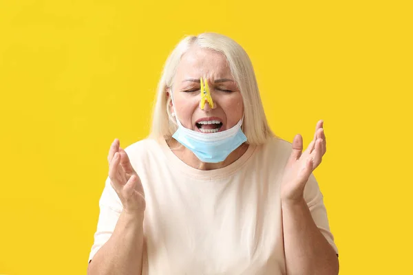 Stressed Mature Woman Clothespin Medical Mask Yellow Background Stuffy Nose — Zdjęcie stockowe