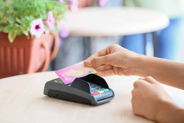 Woman paying with credit card via payment terminal at table in outdoor cafe, closeup