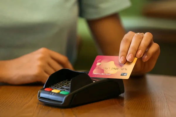 Woman paying with credit card via payment terminal at table in cafe, closeup