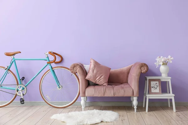 Bicycle, armchair, stepladder with flowers in vase and picture near lilac wall