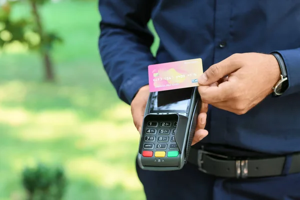 Man paying with credit card via payment terminal outdoors, closeup
