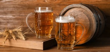 Mugs of fresh beer and barrel on wooden background. Oktoberfest celebration
