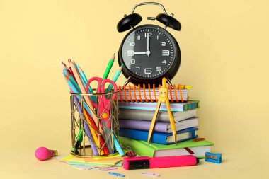 Pen cup with school stationery, books and alarm clock on yellow background