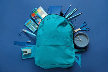 School backpack with stationery on blue background