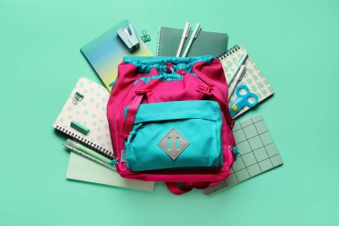 Yeşil arka planda kırtasiye malzemesi olan okul çantası