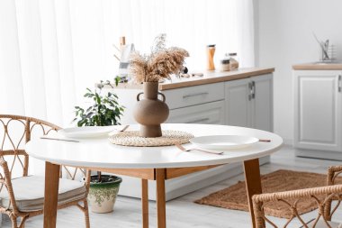 Vase with pampas grass and dishes on dining table in cozy kitchen