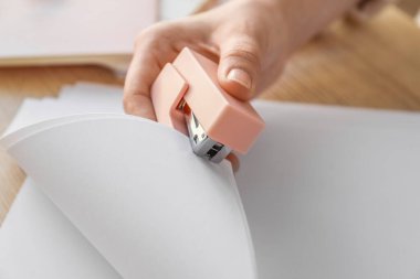 Woman with stapler and paper sheets at table, closeup