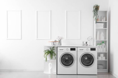 Interior of light laundry room with washing machines and shelving units