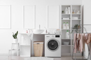 Interior of light laundry room with washing machine, sink and shelving units