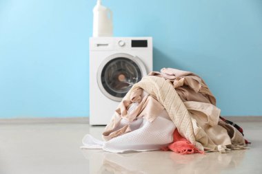 Stack of clothes and washing machine with detergent near blue wall