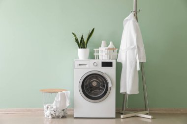 Interior of stylish laundry room with washing machine, rack and bathrobe