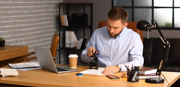 Male notary public attaching seal to document in office