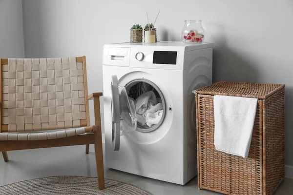 Interior of modern laundry room with washing machine, armchair and basket