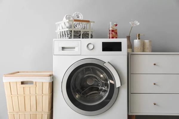 Washing machine with basket, towels and capsules near light wall in laundry room