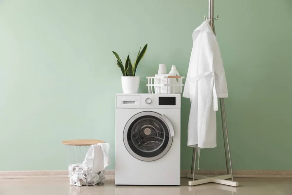 Interior of stylish laundry room with washing machine, rack and bathrobe