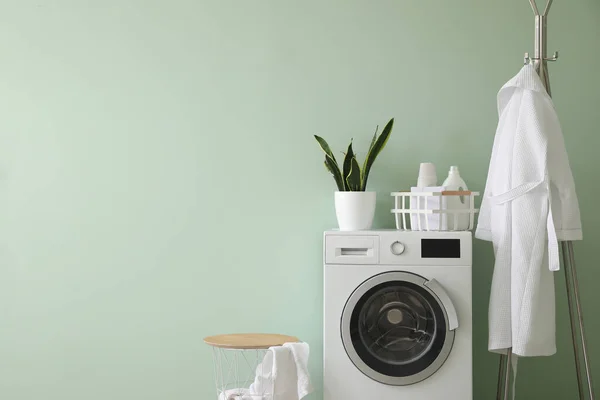 Interior of stylish laundry room with washing machine, rack and bathrobe
