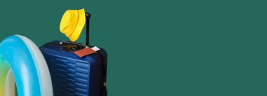 Suitcase, inflatable ring and beach accessories on green background with space for text